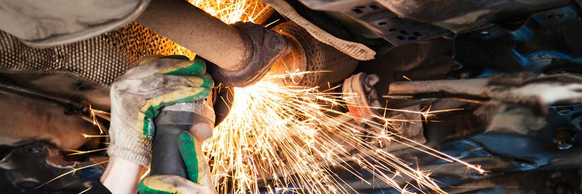 A person uses an angle grinder to cut a car's exhaust system.