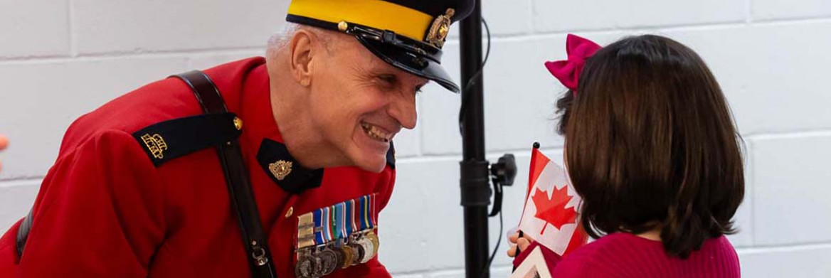 Young girl receives Canadian flag from a male Mountie in red serge.