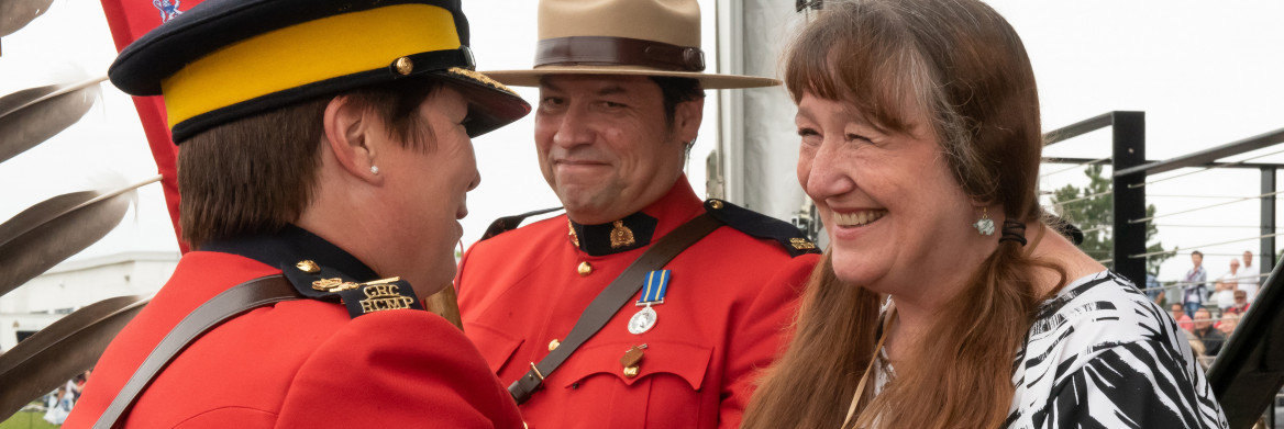 Female RCMP officer in red serge holds hand with a woman, with a male RCMP officer in red serge looking on.