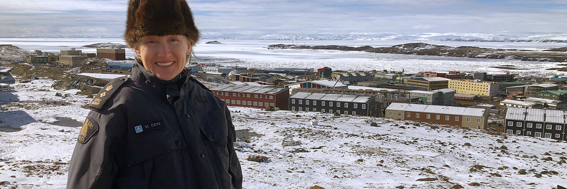 A female RCMP officer looks at the camera. A snow-covered town is in the background.