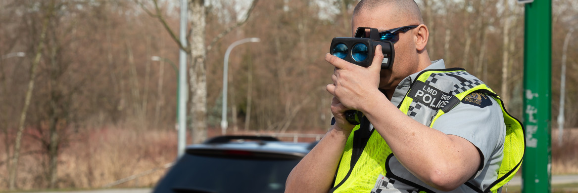 Male police officer on a street looking through speed detector.