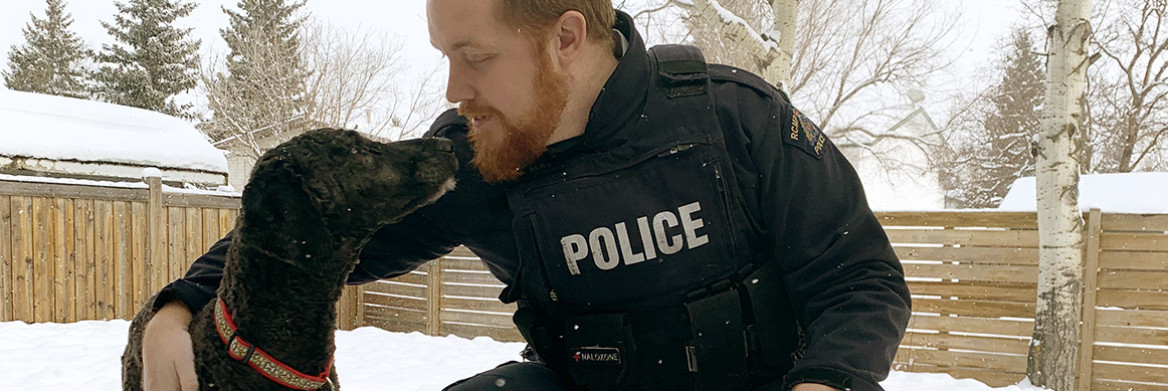 An RCMP officer in uniform poses with a dog. 