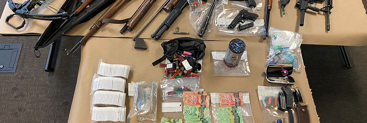 A variety of seized items, spread out on a floor, including a variety of firearms, knives, drugs and cash.
