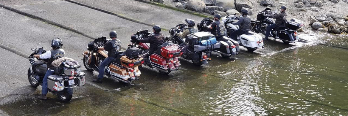 A group of motorcycle riders sit on their bikes with the rear tires slightly in the water.
