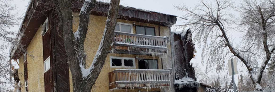A small apartment building is covered in plywood with icicles covering each balcony.