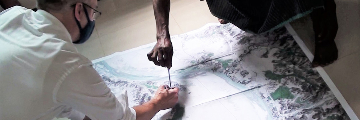 A man wearing a mask and a woman examine a large topographical map on a floor.